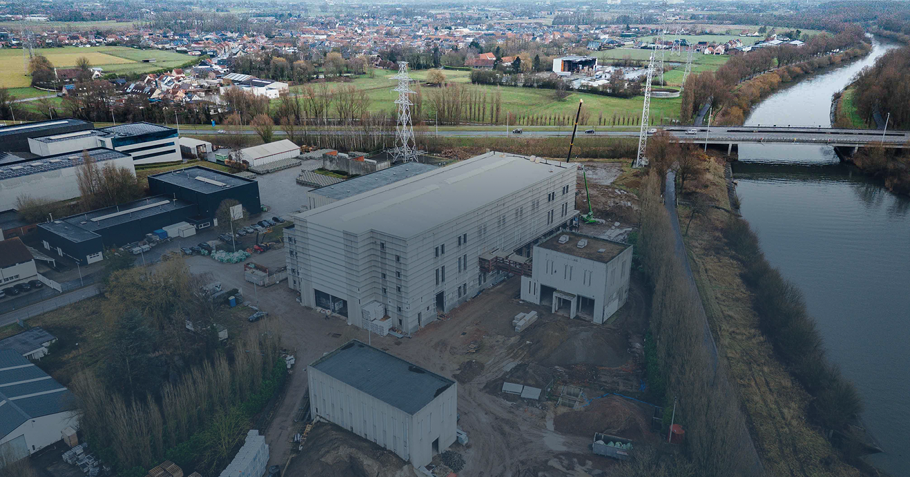 Een luchtfoto van een omvangrijke industriële projectsite aan een kanaal, waar Kristof Devalckenaere verantwoordelijk is voor de technische inrichting, beveiliging en energie-infrastructuur van de bedrijfsgebouwen.