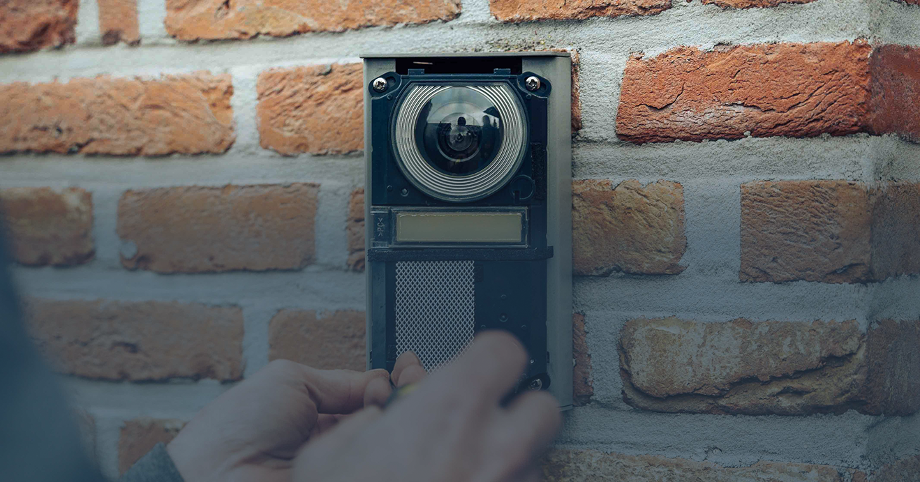 Close-up van de installatie van een Akuvox video-intercom met groothoekcamera op een bakstenen gevel, vakkundig gemonteerd door installateur Kristof Devalckenaere.