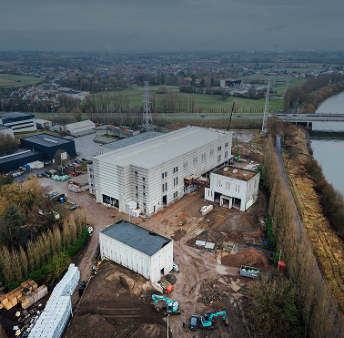 Een luchtfoto van een omvangrijke industriële projectsite aan een kanaal, waar Kristof Devalckenaere verantwoordelijk is voor de technische inrichting, beveiliging en energie-infrastructuur van de bedrijfsgebouwen.