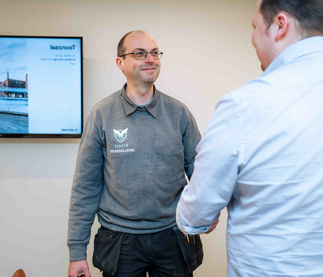 Kristof Devalckenaere verwelkomt een klant hartelijk in zijn moderne toonzaal voor persoonlijk en deskundig advies over beveiliging, domotica en technische installaties.