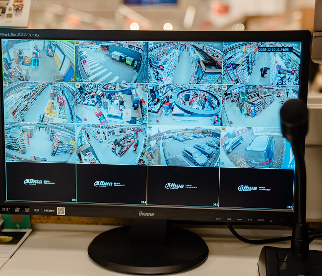 Een monitor toont live beelden van meerdere Dahua beveiligingscamera's in een winkel, inclusief parkeerplaats en gangpaden, geconfigureerd door Kristof Devalckenaere.