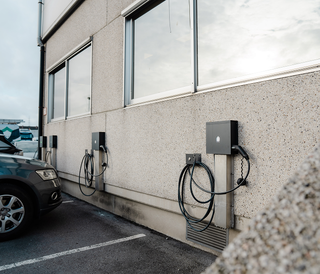 Een rij zwarte Smappee EV-laadpalen gemonteerd op de buitengevel van een kantoorpand voor slim energiebeheer, vakkundig geïnstalleerd door Kristof Devalckenaere.