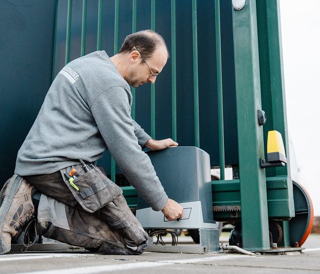 Vakkundig onderhoud van een elektrische schuifpoort door Devalckenaere Kristof. De technicus inspecteert het aandrijfmechanisme om een lange levensduur en optimale werking te garanderen.