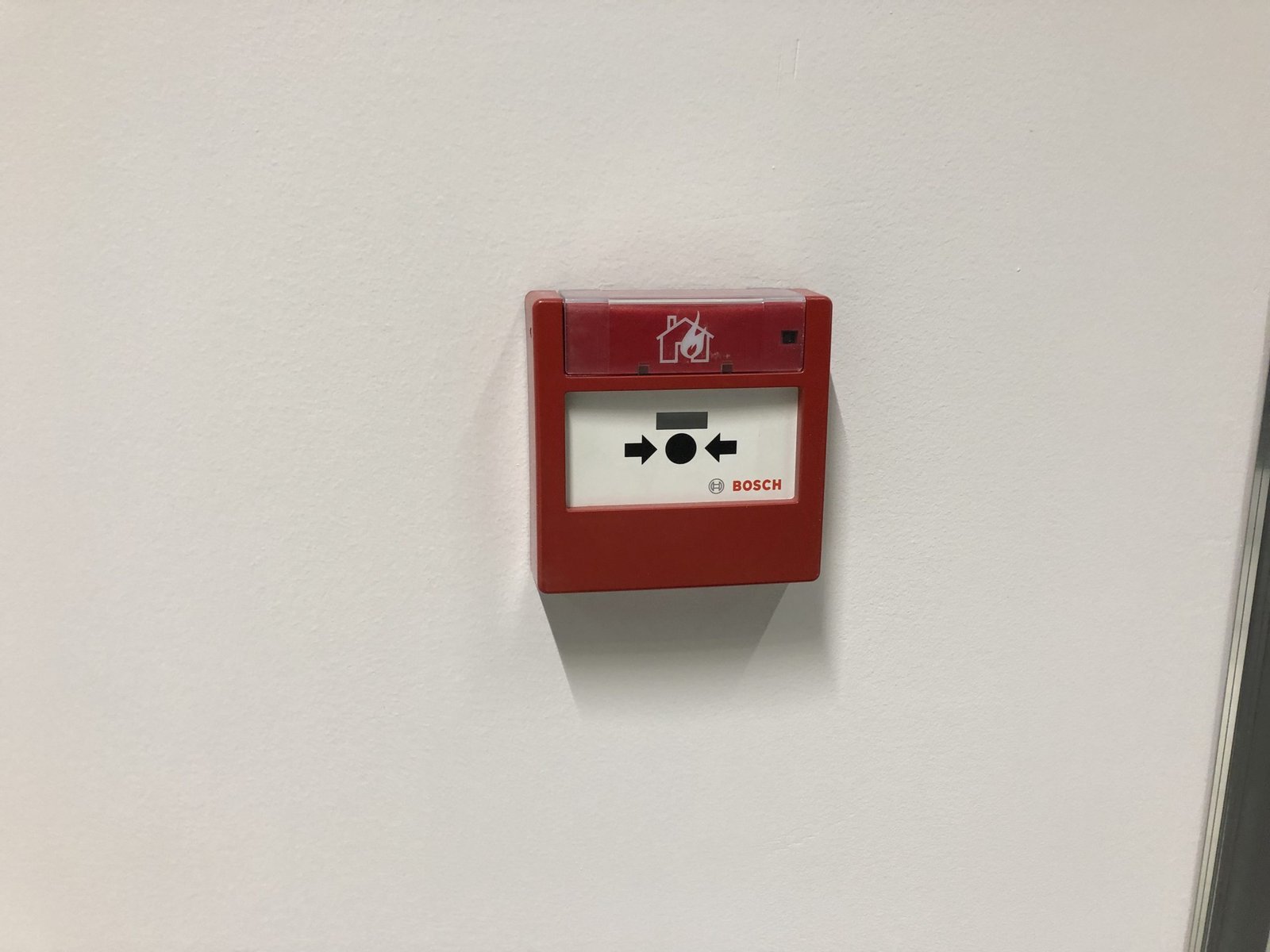 Een rode Bosch handbrandmelder gemonteerd op een witte wand als onderdeel van een professioneel brandbeveiligingssysteem door Kristof Devalckenaere.
